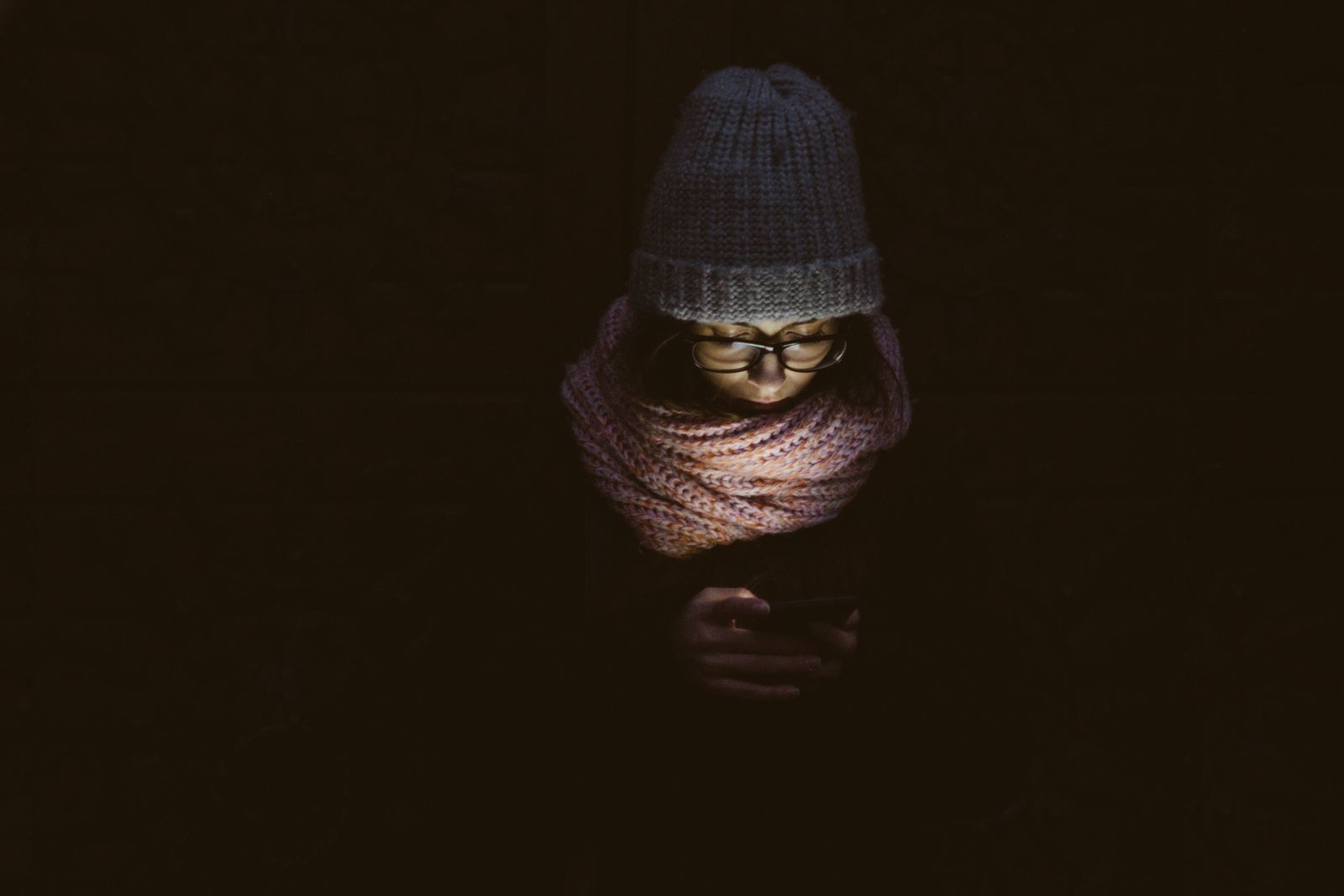 Eine Frau mit Strickmütze und Schal, im Dunkeln nur vom Licht ihres Smartphones beleuchtet