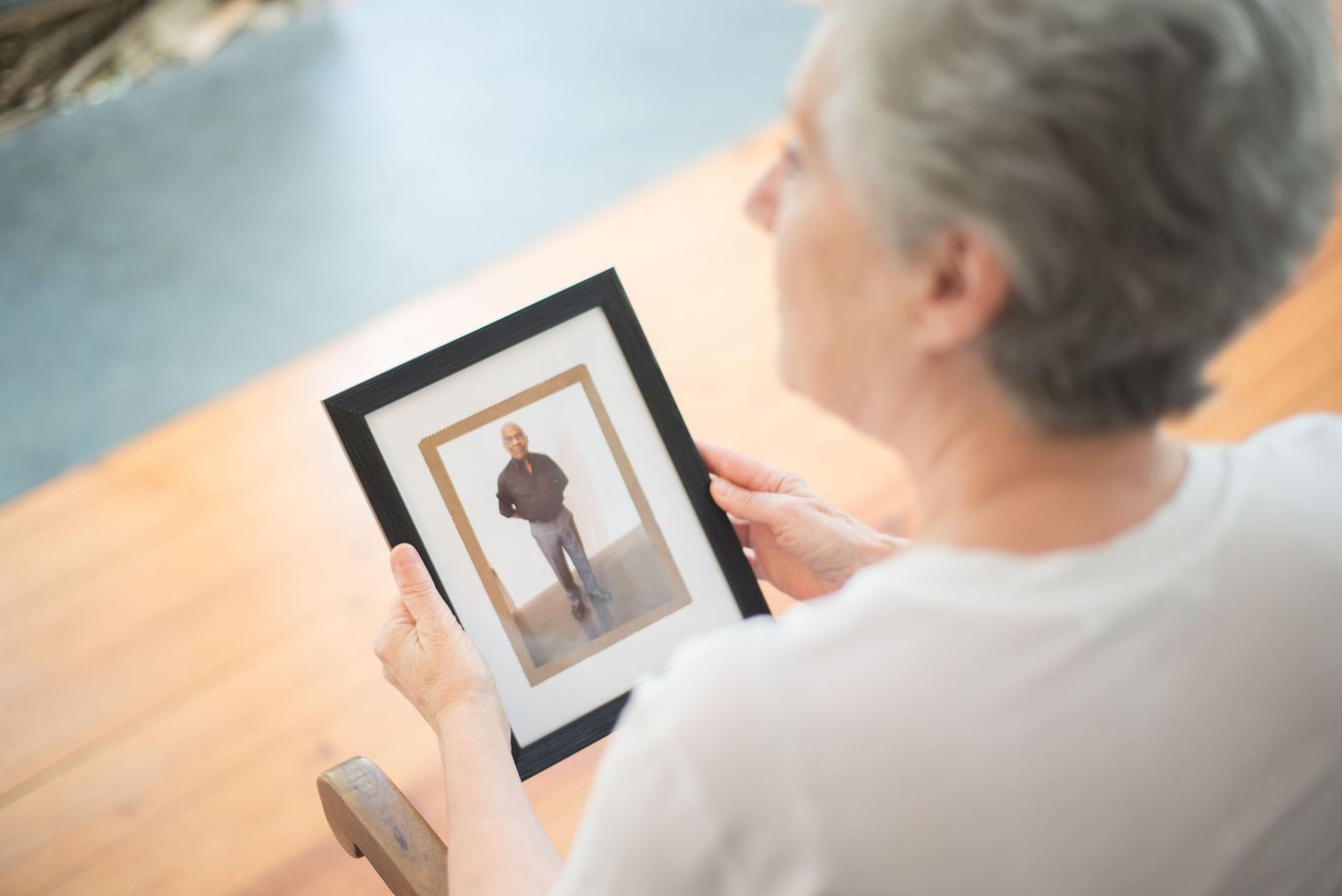 An older woman holding a framed photograph of a man, seen from over her shoulder