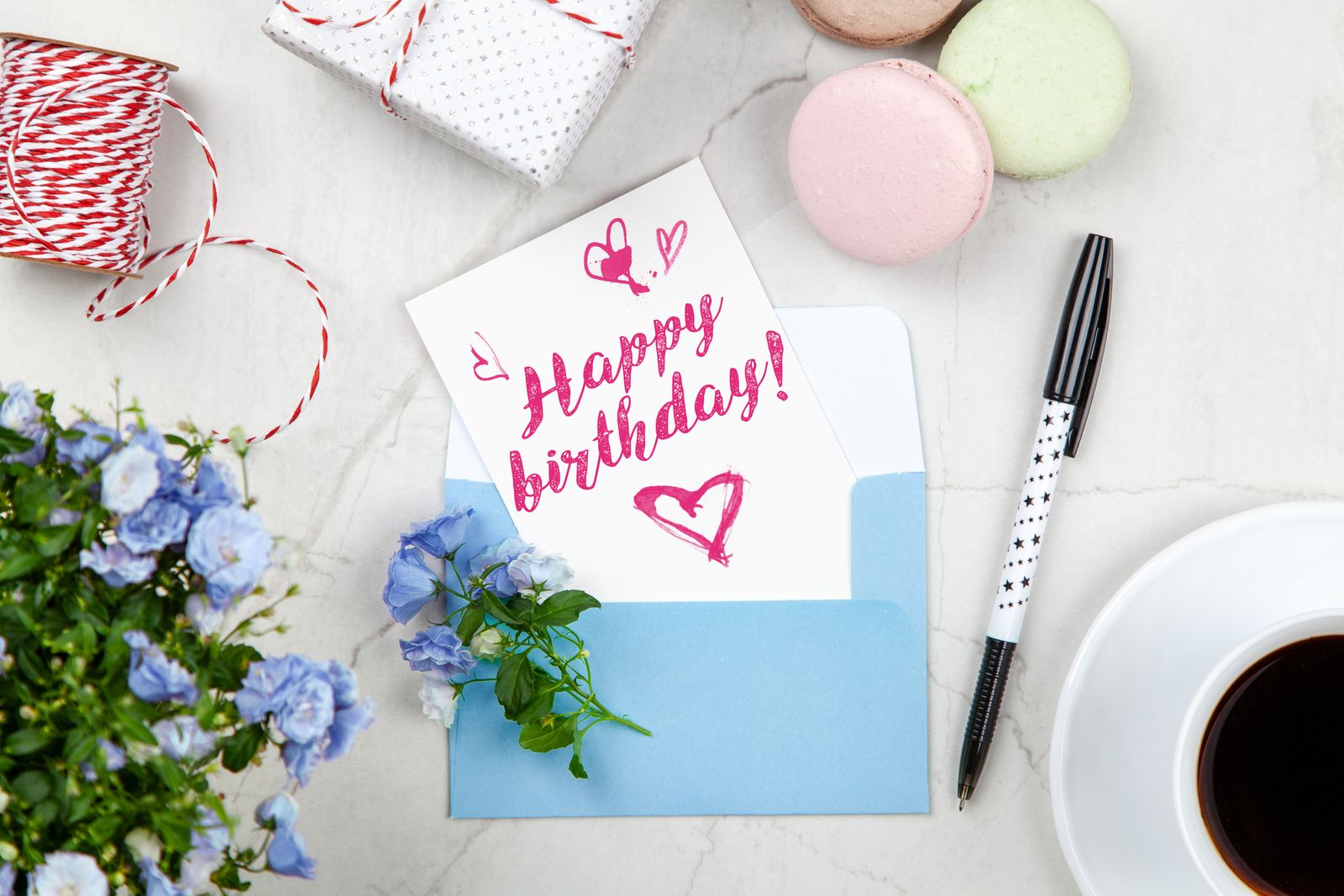 A handwritten happy birthday card tucked into a blue envelope beside flowers and a cup of coffee