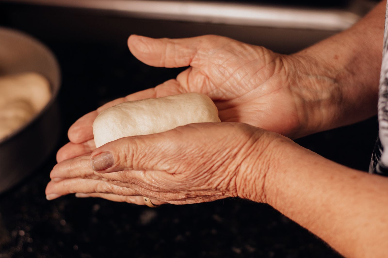 An older woman's hands shaping a ball of soft dough over a dark kitchen counter