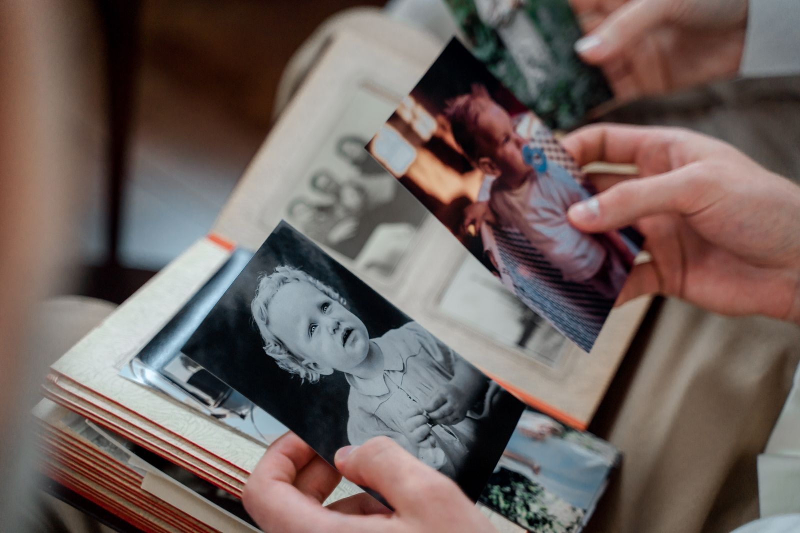 Hände halten alte Familienfotos über einem aufgeschlagenen Fotoalbum