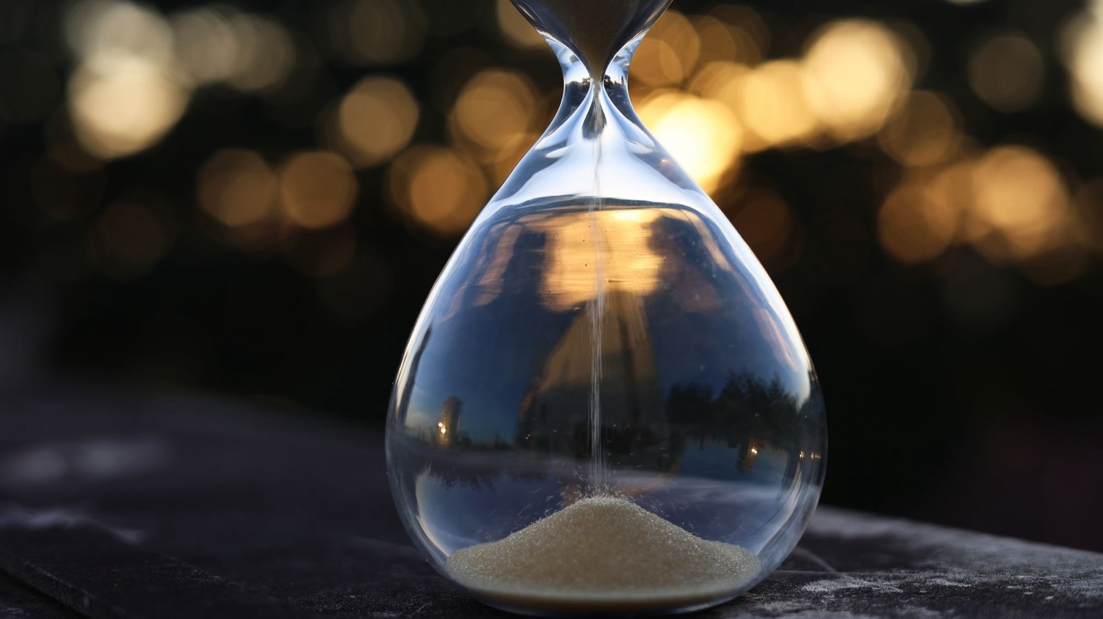 A glass hourglass with sand falling, backlit by a golden sunset