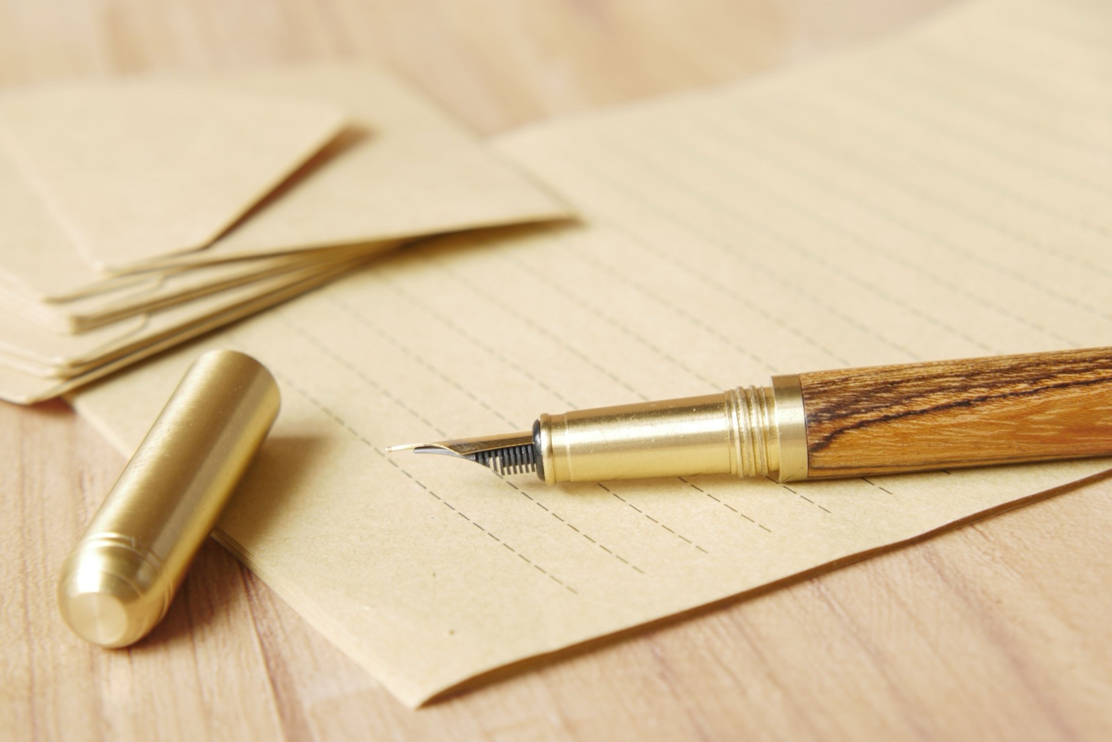 Ein Füllfederhalter aus Gold und Holz liegt in warmem Licht auf liniertem Packpapier neben braunen Umschlägen