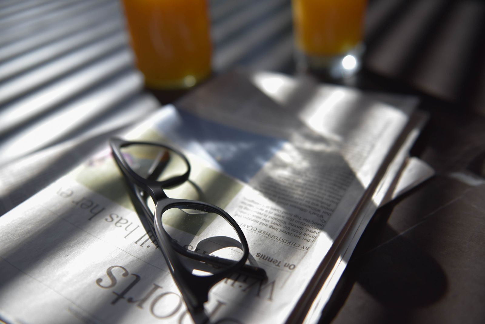Eine Brille liegt auf einer gefalteten Zeitung neben einem Glas Orangensaft