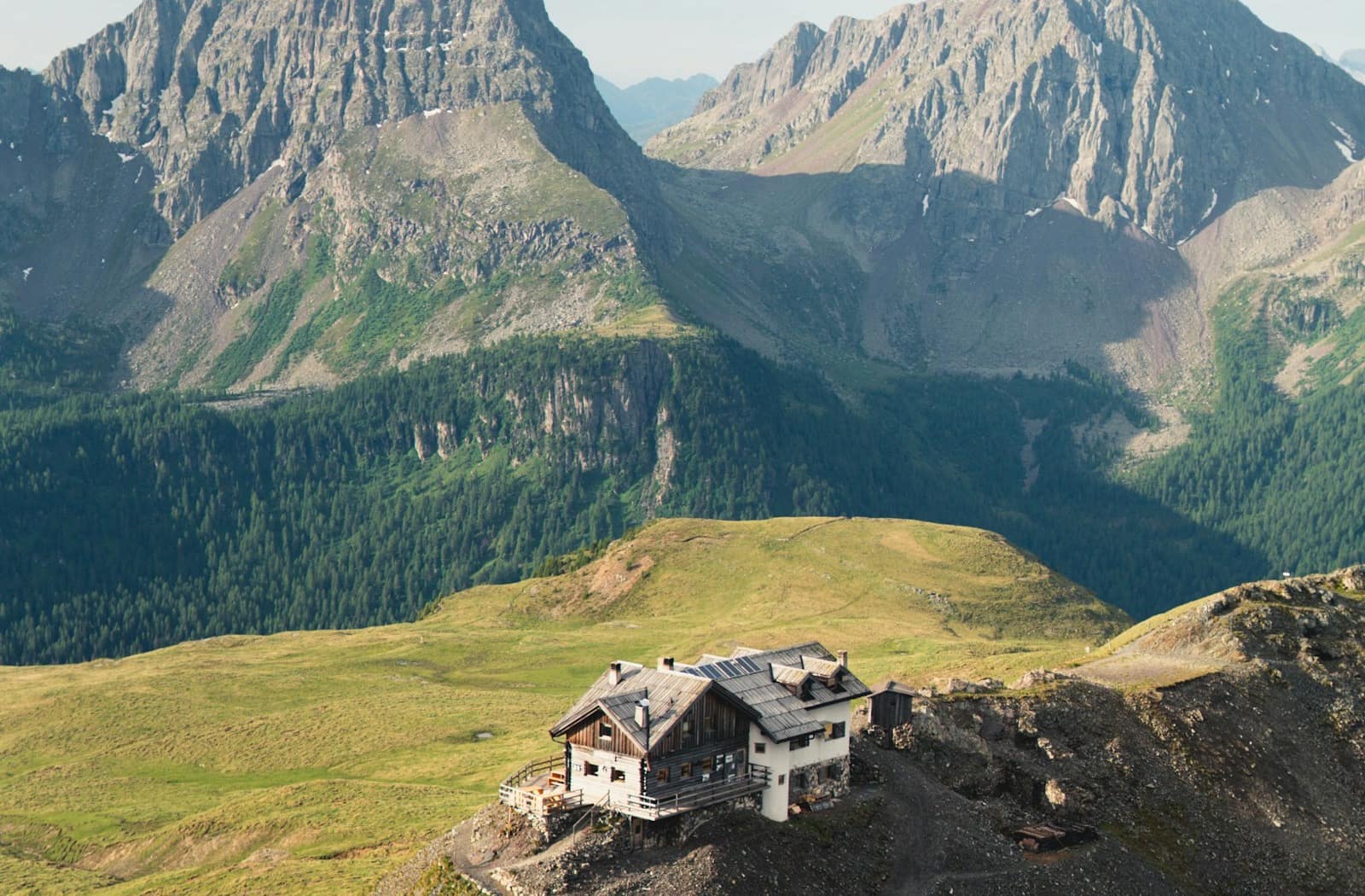 Eine kleine Berghütte auf einem felsigen Grat, dahinter verblassen ferne Gipfel am Horizont