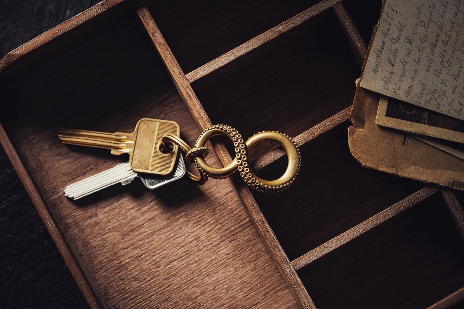Brass keys on a keyring lying in a wooden keepsake box beside old handwritten letters
