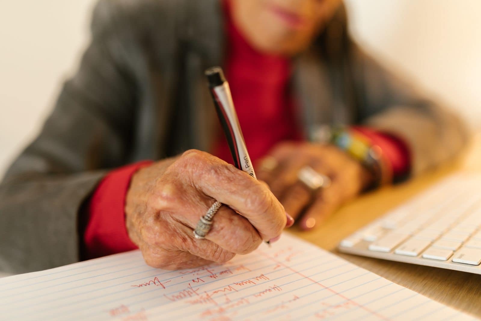 Eine alte Hand mit silbernem Ring schreibt mit einem Stift auf liniertem Papier