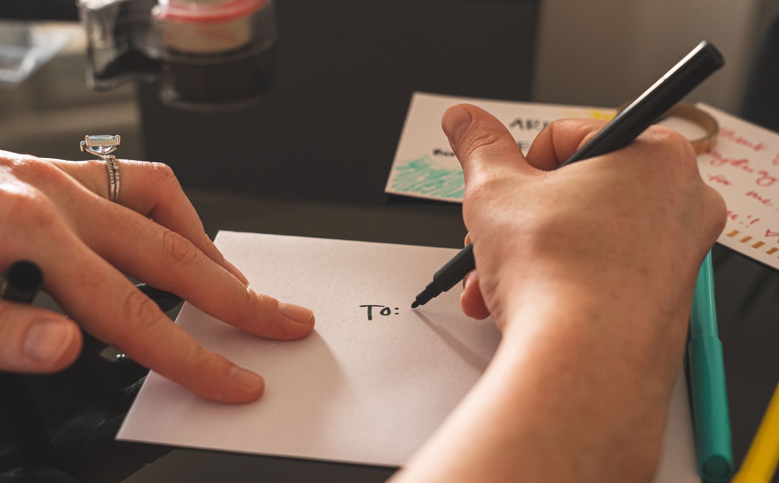 A hand writing on a sealed envelope at a desk beside a stack of blank envelopes