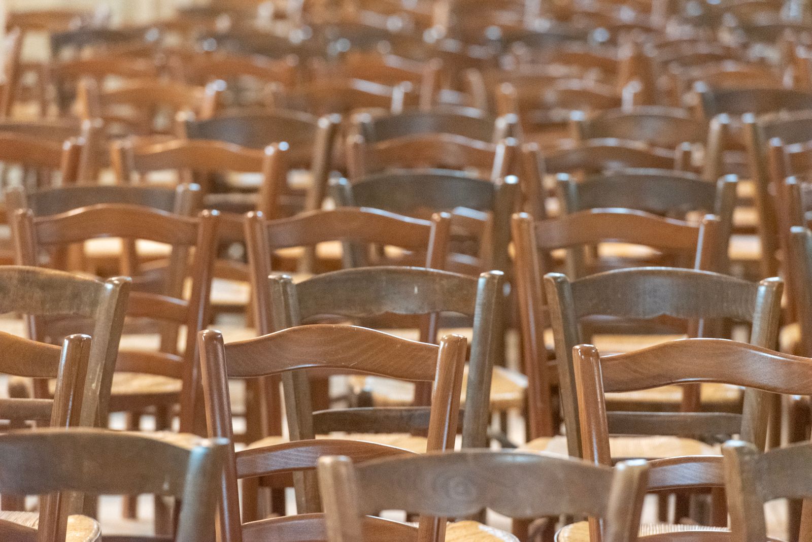 Rows of empty wooden chairs in a quiet hall lit by soft daylight