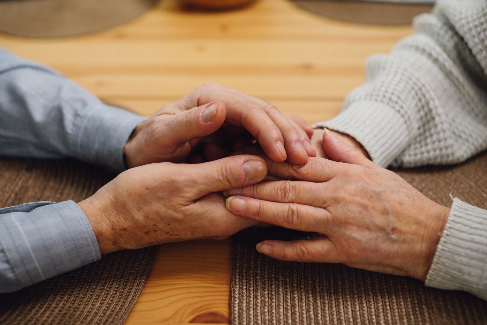 Two older people holding hands across a wooden kitchen table