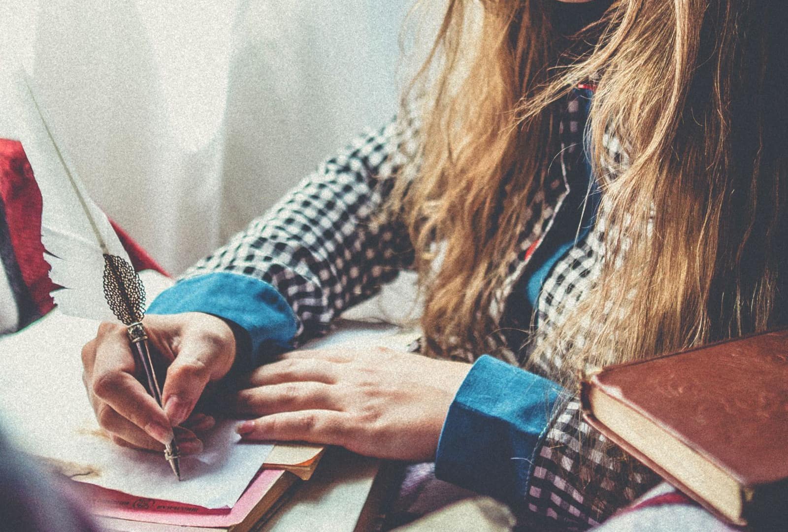 يدان تكتبان رسالة بريشة كتابة إلى جانب كومة من الكتب القديمة
