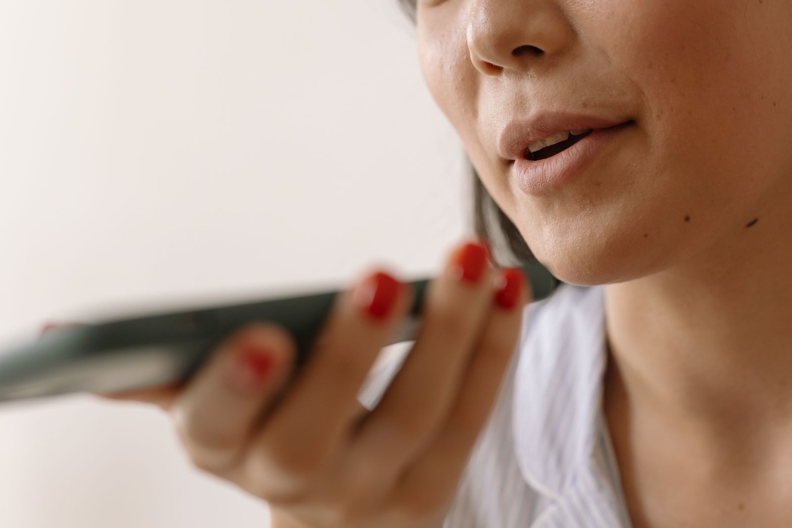 A woman holding a phone close to her chin, speaking into the microphone end of it